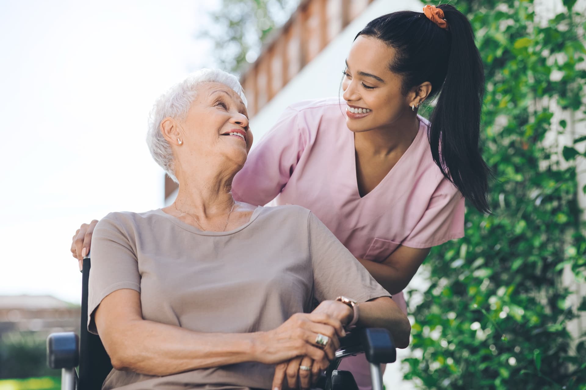 Cuidadora sonriendo a una señora mayor en silla de ruedas en un jardín